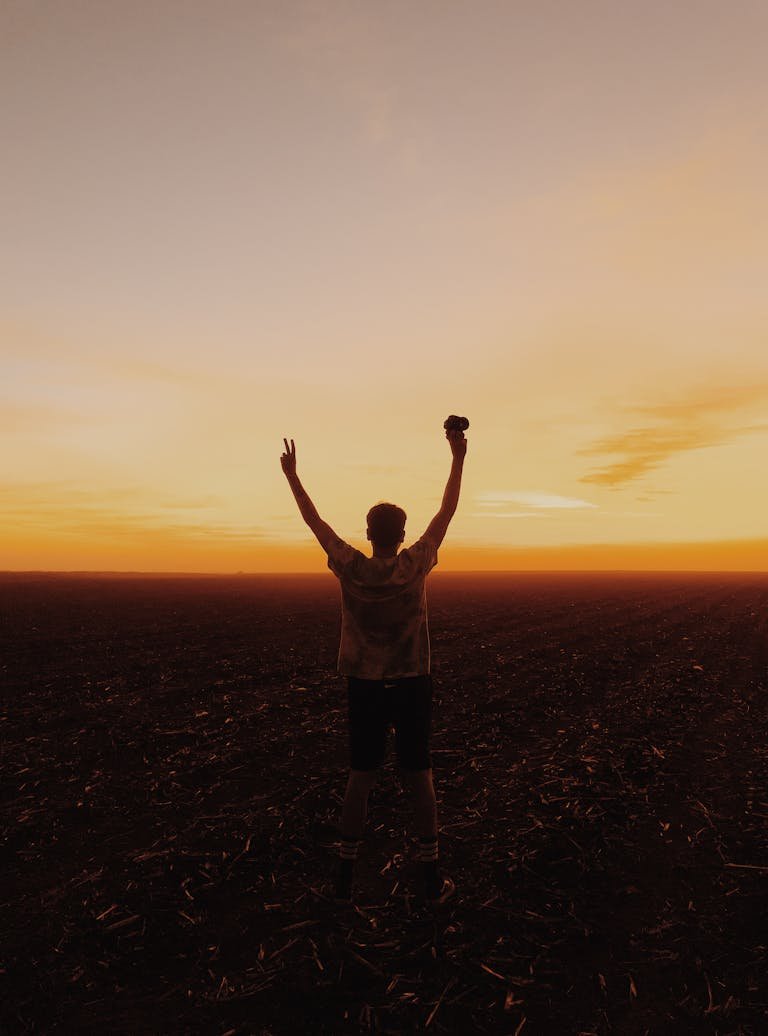 Silhouette of Man with Hands Up in Field on Sunset